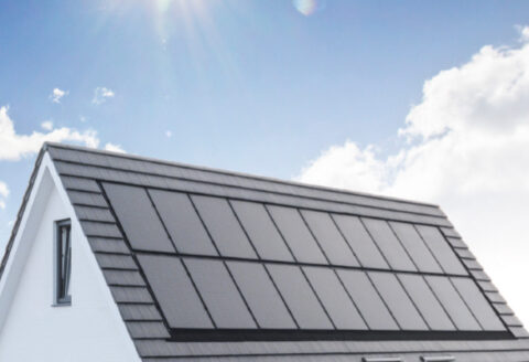 Das schwarze Dach eines Hauses mit PV-Modulen vor hellem blauen Hintergrund